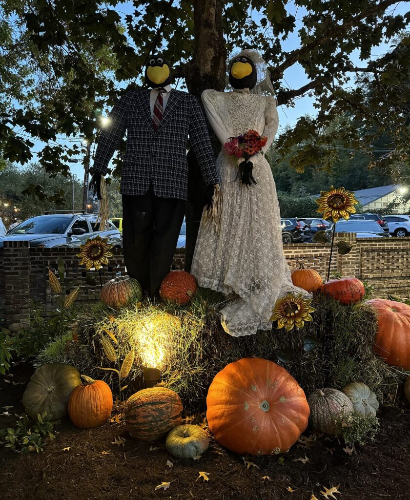 A scarecrow bride and groom with crow faces stand on hay bales surrounded by pumpkins at The Village Shops in downtown Gatlinburg