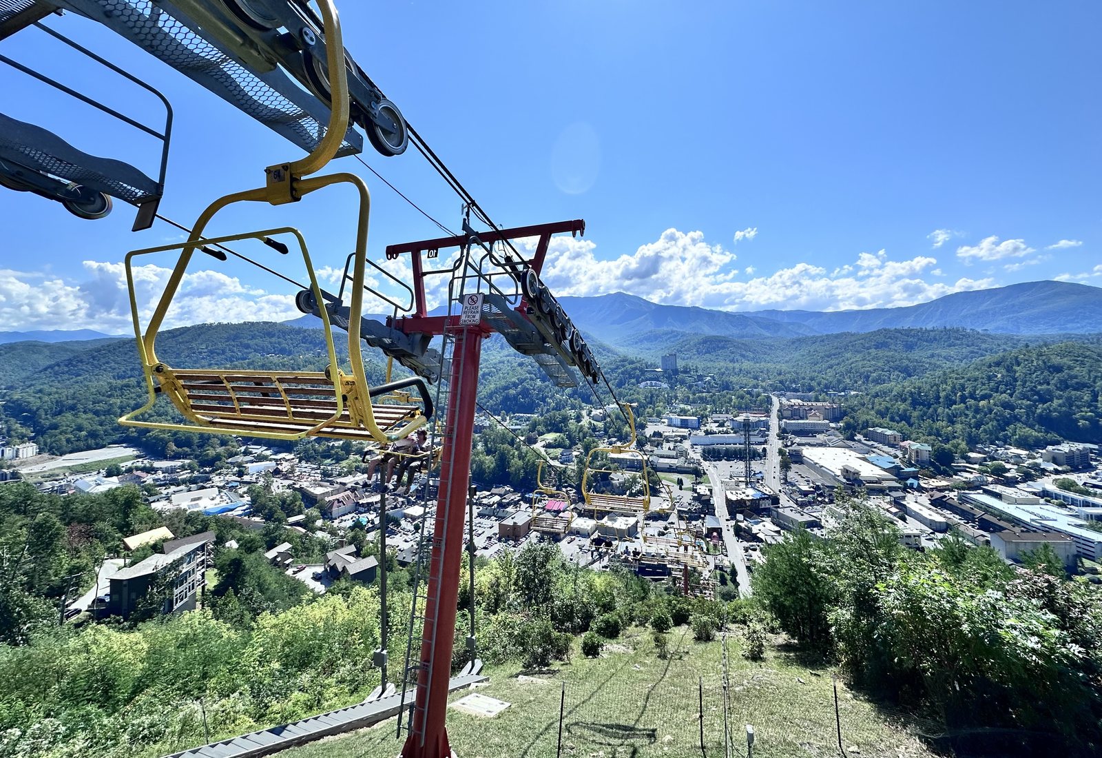 Yellow SkyLift chairs climb the hillside at Gatlinburg SkyPark, with downtown Gatlinburg and the Great Smoky Mountains under a blue sky behind them.