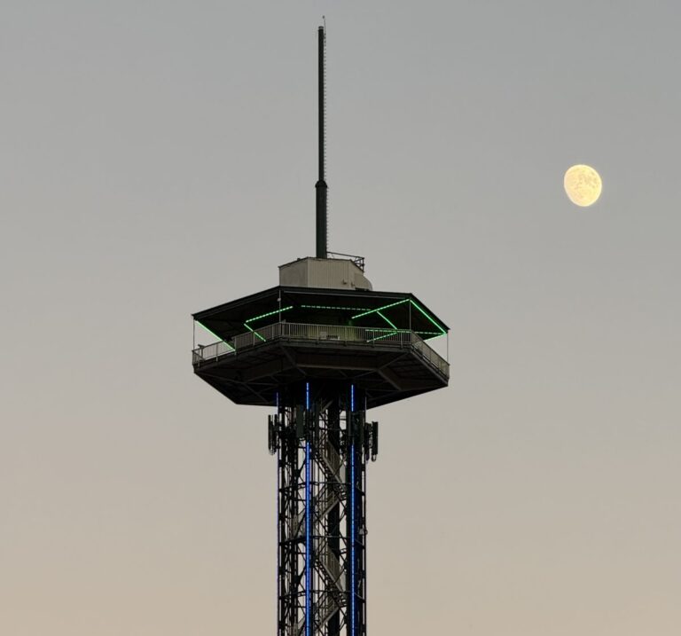 The top of the Gatlinburg Space Needle observation tower against an evening sky with the moon beside it