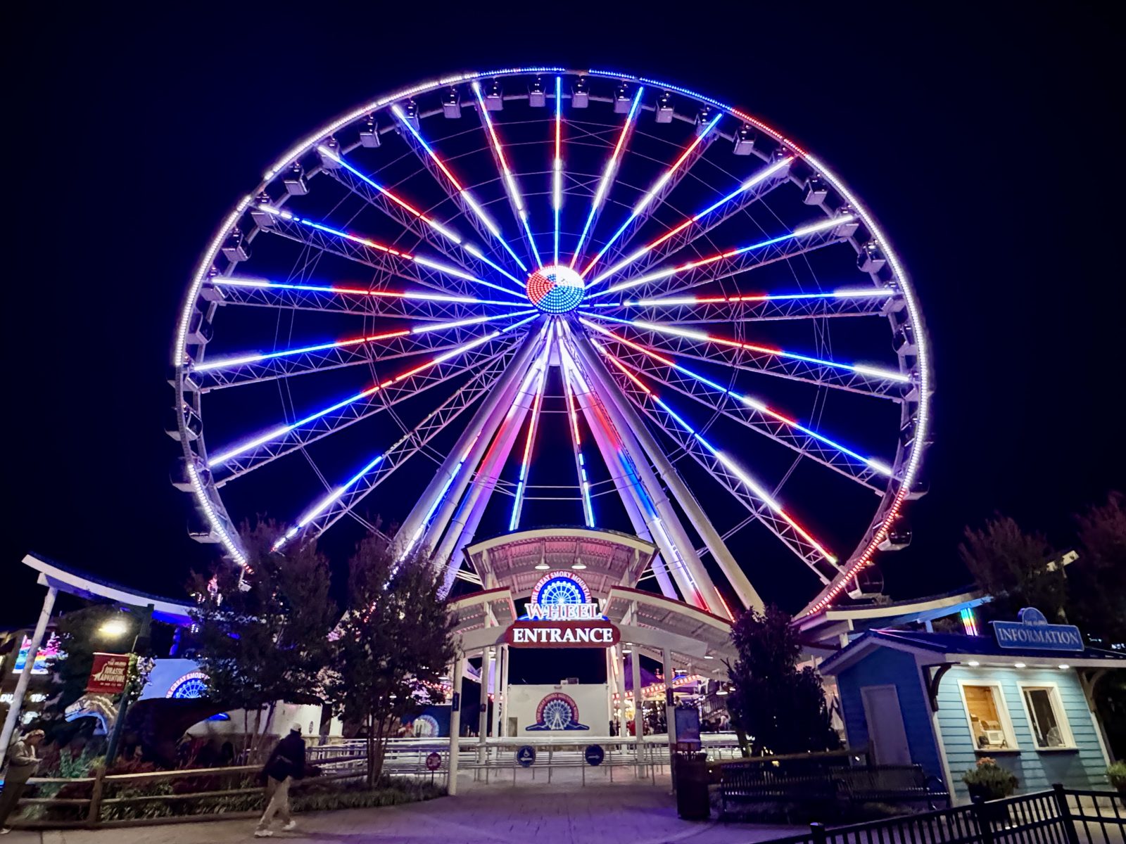 The Great Smoky Mountain Wheel at The Island in Pigeon Forge lit up in red, white and blue at night above the wheel entrance