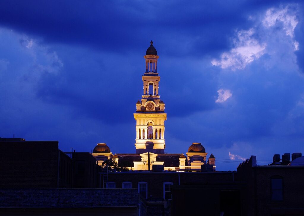 The clock tower of the Sevier County Courthouse glows with light against a deep blue evening sky above the rooftops of downtown Sevierville.